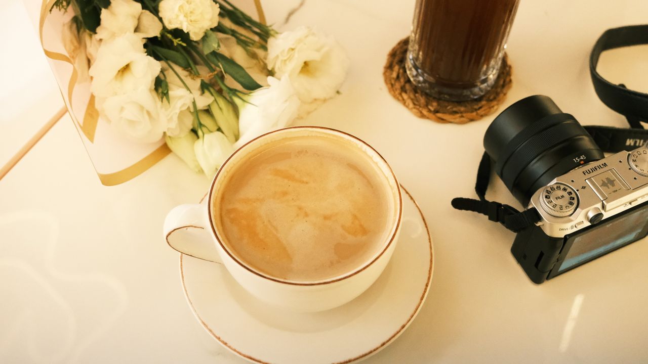 Mastering the First Impression: Your intriguing post title goes here Relaxing coffee break setup with cappuccino, flowers, and camera on a clean white table.