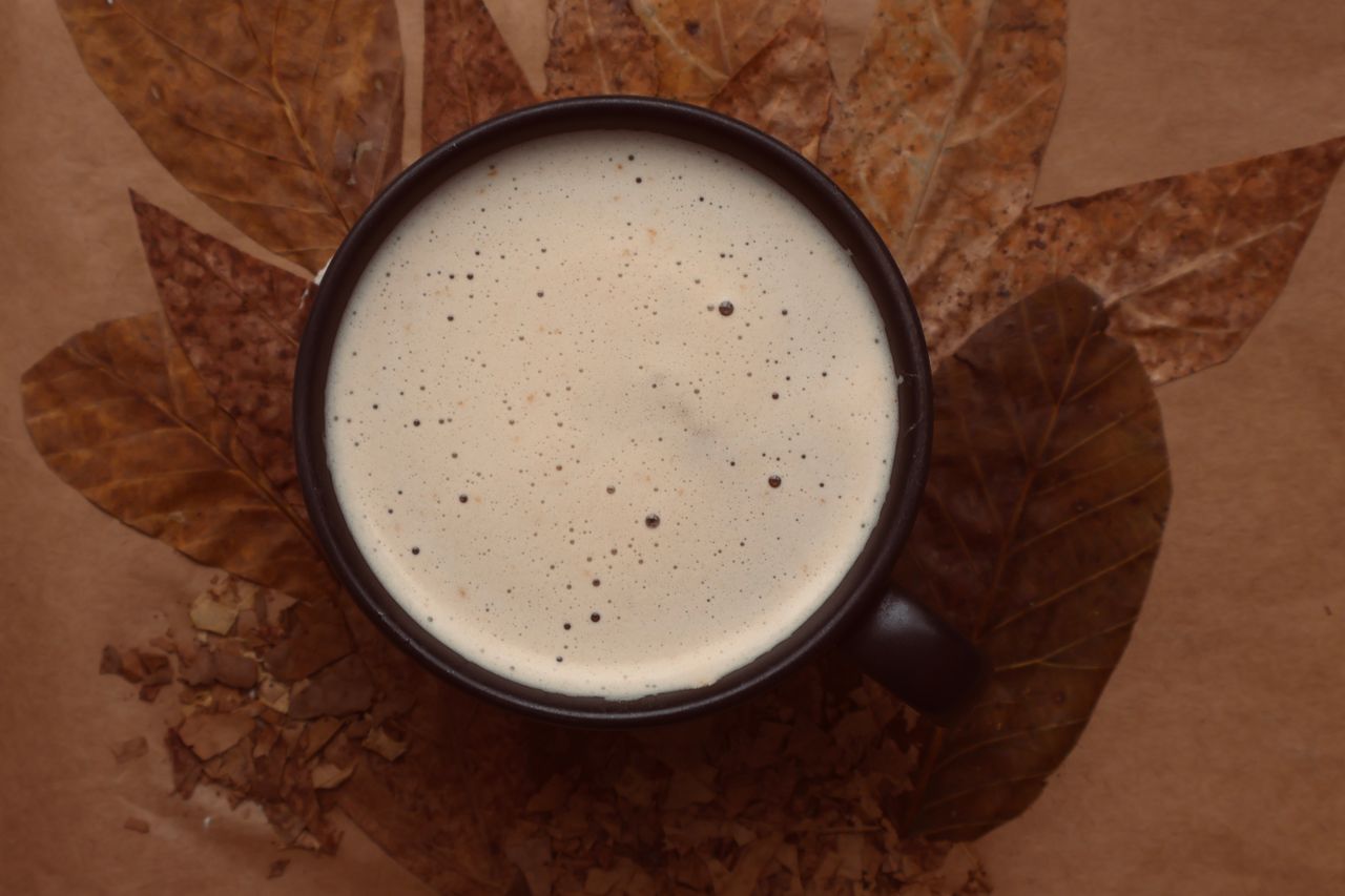 Top-down view of a frothy coffee cup placed on autumn leaves creating a cozy fall ambiance.